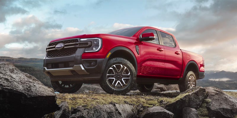 Red Ford pickup truck parked on rocky terrain with mountains in the background. 