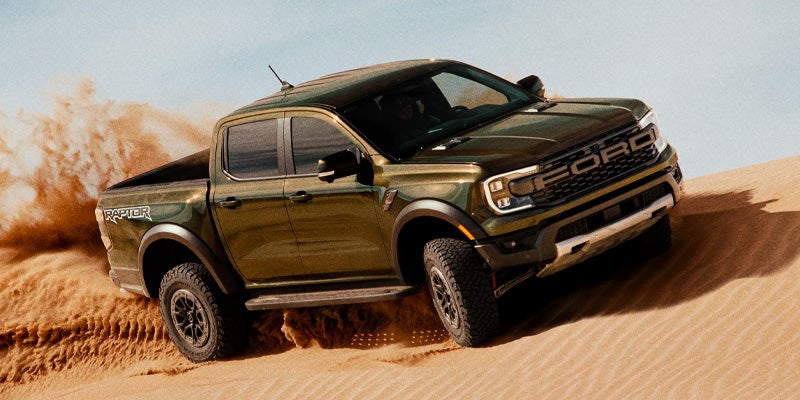 Green Ford Raptor pickup truck driving through sand dunes.
