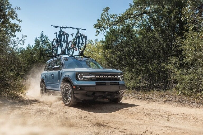 A Ford Bronco Sport driving on a dirt road with bikes attached on top