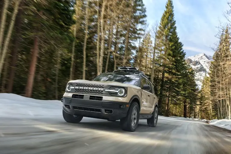 A Ford Bronco Sport driving on a paved road with snow on the banks