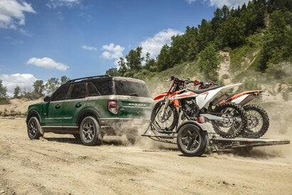 A Ford Bronco Sport driving on a dirt road while carrying two bikes on a trailer