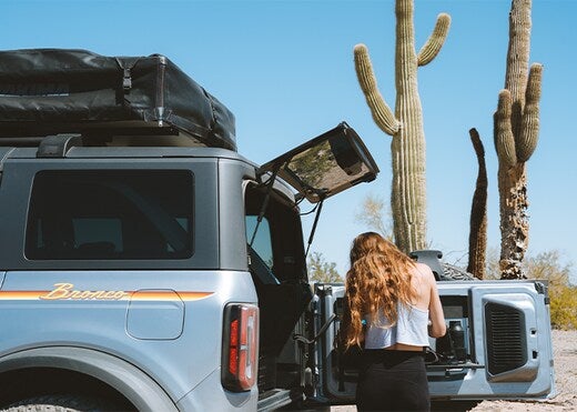a ford vehicle in a desert terrain with the a woman behind the hatchback door