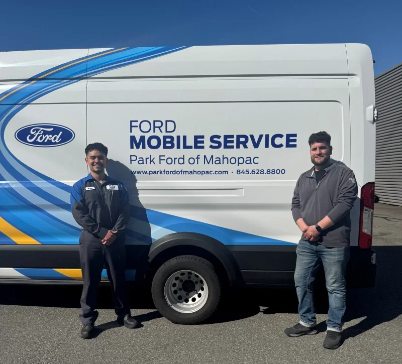 Two men standing beside a white Ford Mobile Service van with blue and yellow accents.