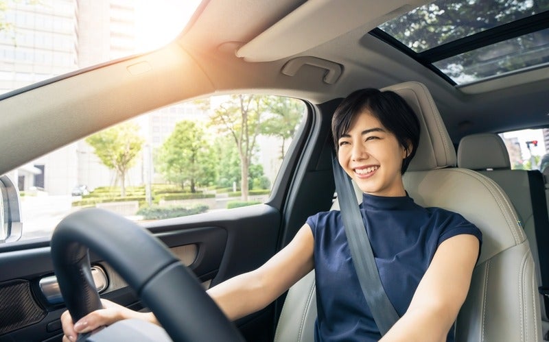 A woman, with her hands on the steering wheel, smiling while looking ahead